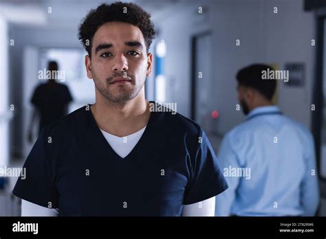 Portrait Of Biracial Male Doctor Standing In Hospital Corridor Stock