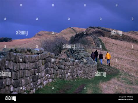 Four People Walk Along Hadrians Wall At Cawfield Crags In