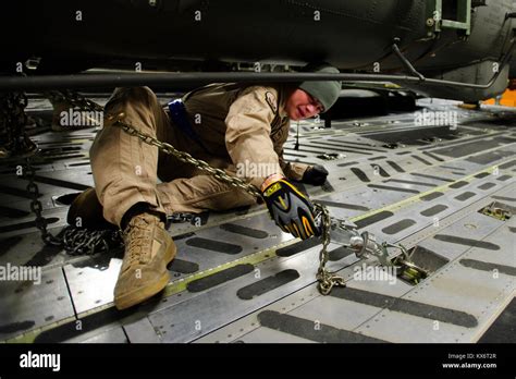 A U.S. Air Force C-17 Loadmaster unchains an AH-64D Apache Longbow to prepare to move off the C ...