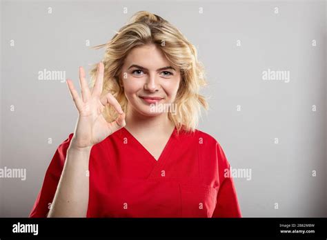 Portrait Of Female Nurse Wearing Red Scrub Showing Ok Gesture On Studio