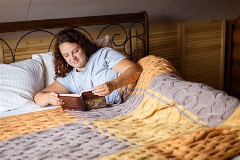 Brunette Woman Lying Under Terry Covers on Bed Holding Book in Hands ...