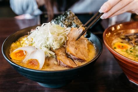 Mão da mulher que comprime o macarronete na sopa do osso da carne de