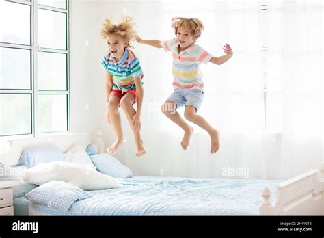 Child jumping on bed in white bedroom with big window. Kids play at home. Fun jump on parents ...