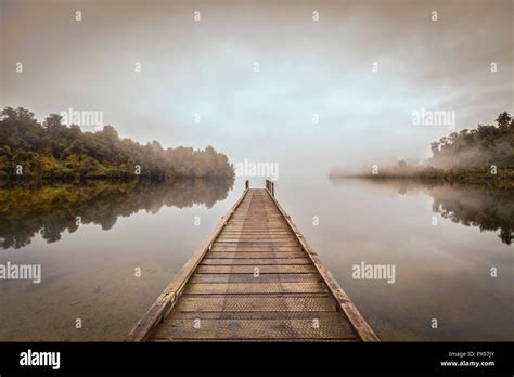 A Jetty On A Calm Lake Mapourika New Zealand With Mist Drifting