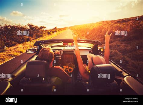 Happy Young Couple Driving Along Country Road In Convertible At Sunset Freedom Adventure