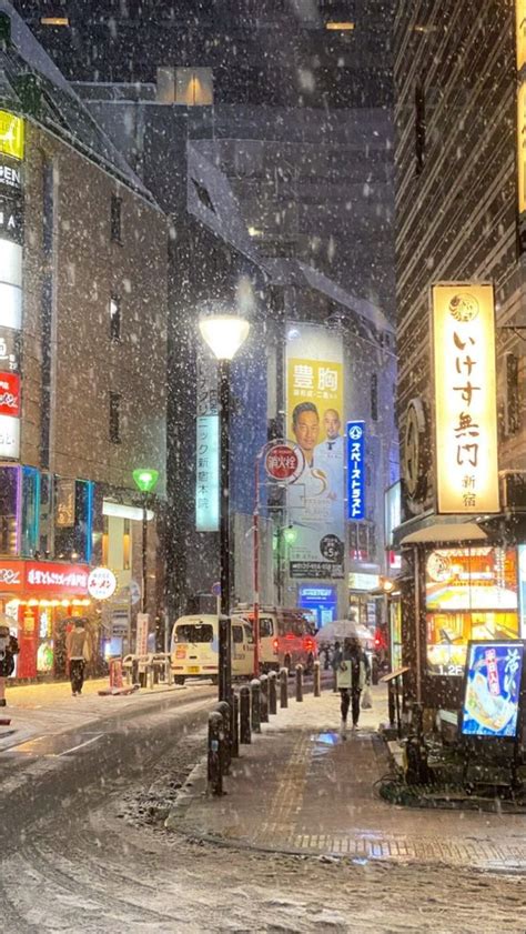 A Person Walking Down A Snowy Street In The City At Night With Snow