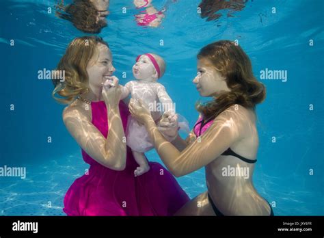 Mamá y dos hijas en vestido rosado posando bajo el agua en la piscina