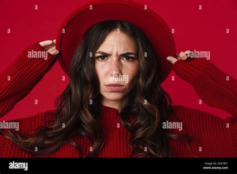 Displeased Beautiful Brunette Girl In Hat Posing And Looking At Camera Isolated Over Red