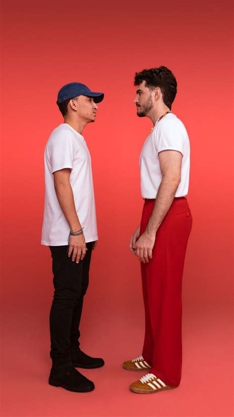 Two Men Standing Next To Each Other In Front Of A Red Background