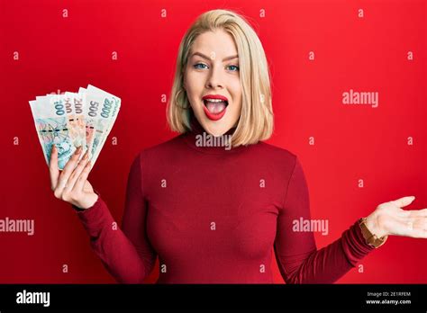 Jeune femme blonde portant des billets de koruna tchèque célébrant son succès sourire heureux et
