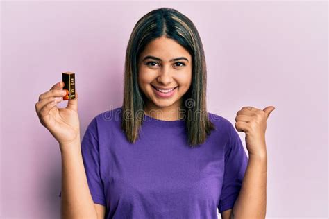 Young Latin Woman Holding Small Gold Ingot Pointing Thumb Up To The