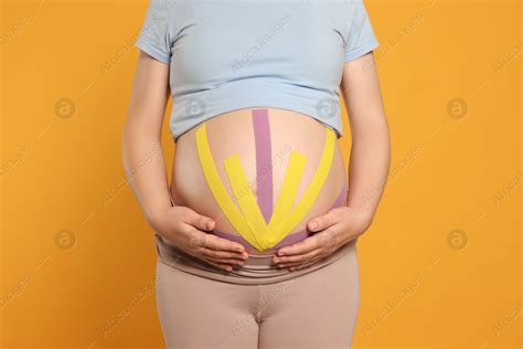 Pregnant Woman With Kinesio Tapes On Her Belly Against Orange