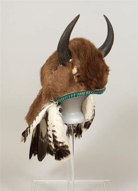 A Taxidermy Head With Horns And Feathers On A Glass Stand In Front Of A