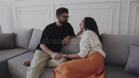 A Man And A Woman Are Sitting On A Couch Holding Hands And Looking At