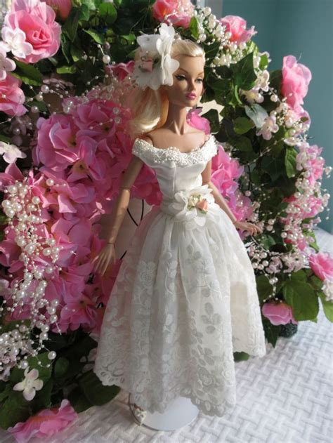 A Barbie Doll Dressed In A White Dress Standing Next To Pink Flowers