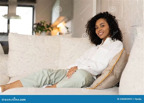 Happy Young African American Woman Sitting On Sofa At Home And Looking