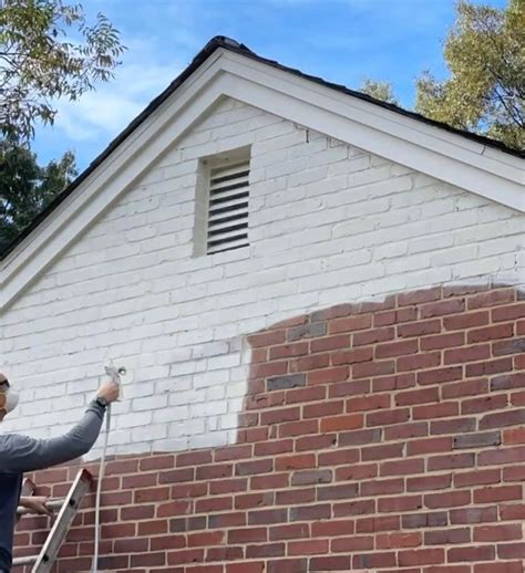 A Man Is Painting The Side Of A Brick Building With White Paint And A