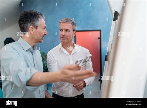Mature Male Coworkers Discussing Over Equipment While Standing By