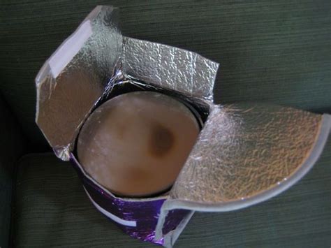 An Open Tinfoil Covered Box Sitting On Top Of A Green Couch Next To A Cup