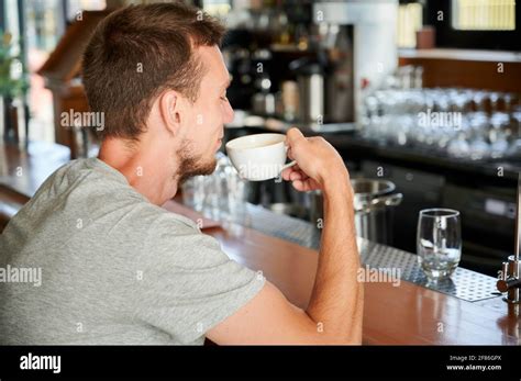 Back View Of Handsome Young Man Sitting On Bar And Drinking Cup Coffee