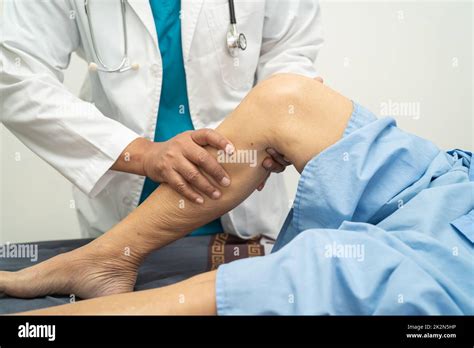 Asian Doctor Physiotherapist Examining Massaging And Treatment Knee