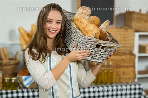 Smiling Female Staff Holding A Basket Of Baguettes At Counter