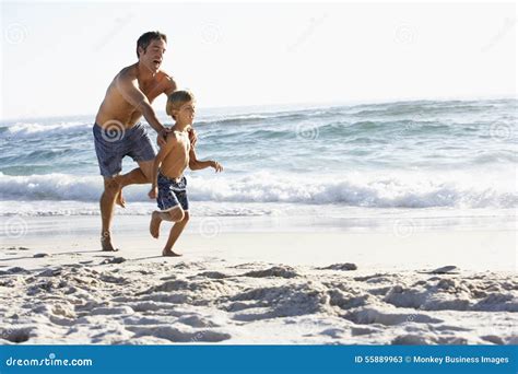 Father And Son Running Along Beach Together Wearing Swimming Costumes