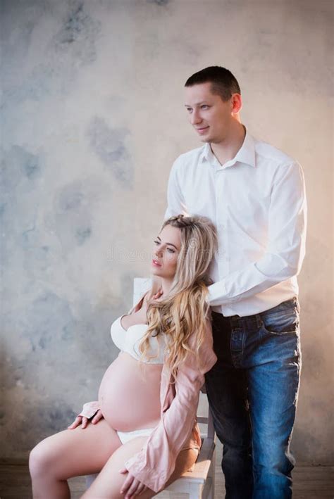 Husband Hugging His Pregnant Wife In White Lingerie On A Light
