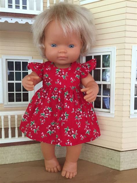 A Doll With Blonde Hair Standing In Front Of A Doll House Wearing A Red Dress