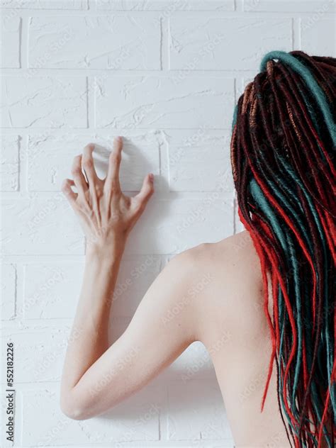 Naked Girl With Long Dreadlocks In Her Hair Standing Near A White Brick Wall With Her Hand
