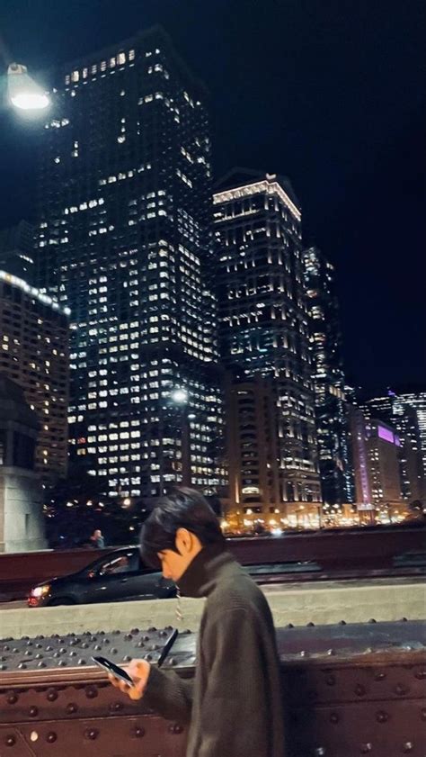 A Man Is Looking At His Cell Phone In Front Of The City Lights And