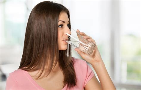 Mujer Joven Bebiendo Agua De Vidrio Sobre Fondo Borroso Foto Premium