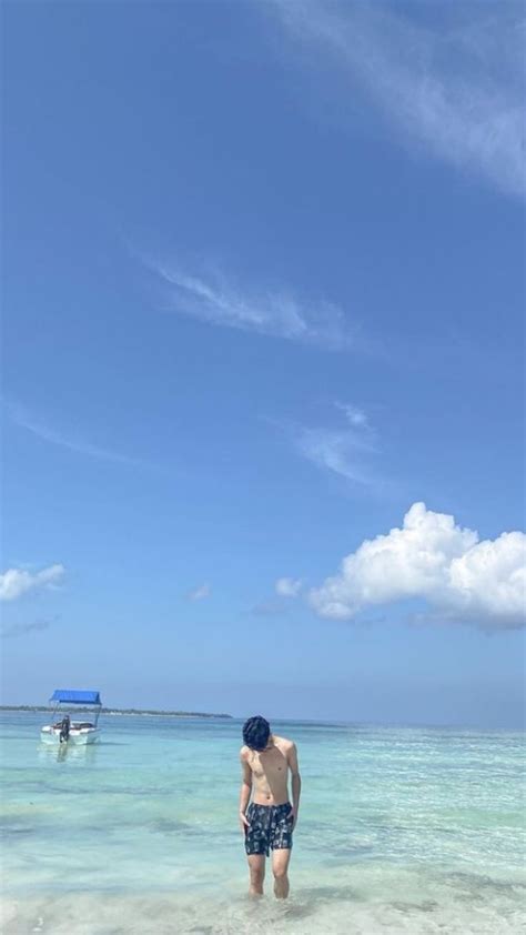 A Man Standing In Shallow Water On The Beach With A Boat In The