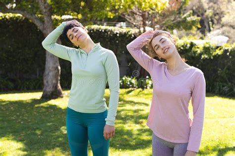 Happy Biracial Lesbian Couple Practicing Yoga Standing And Stretching Necks In Sunny Garden