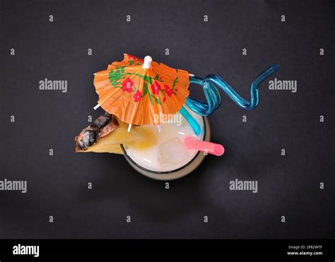 A Tall Glass With A Pina Colada Beach Cocktail On A Black Background With Ice Straws And An