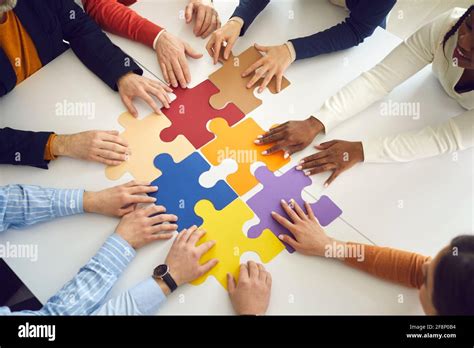 Office Team Assembling Jigsaw Puzzle Pieces On Table Top View On Hands