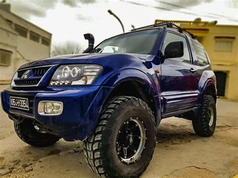 A Blue Truck Parked On Top Of A Dirt Road Next To A Yellow Building In