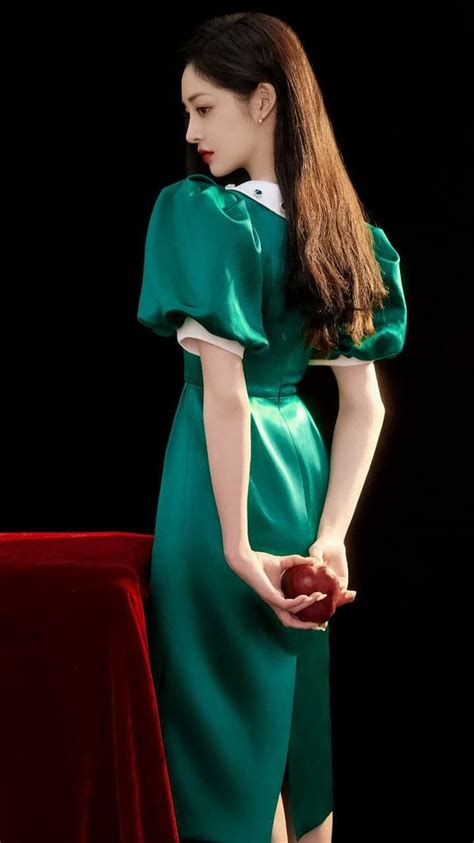 A Woman In Green Dress Holding An Apple Next To A Red Velvet Tablecloth