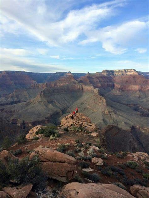 Two People Are Standing On The Edge Of A Cliff At The Grand Canyon In