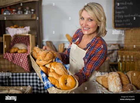 Smiling Female Staff Holding Wicker Basket Of Various Breads At Counter