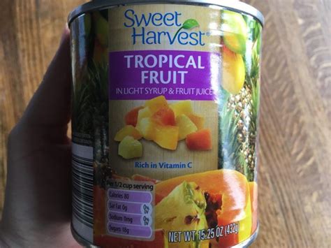 A Can Of Sweet Harvest Tropical Fruit Sits In Someone S Hand On A