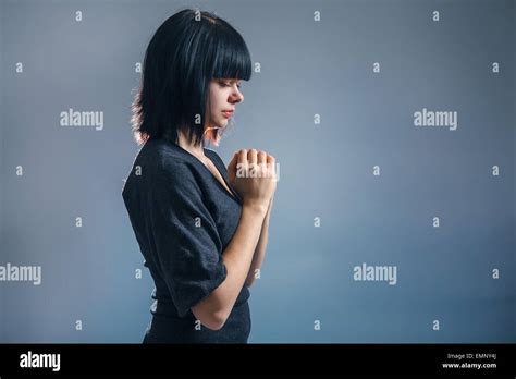 European Appearance Brunette Girl Clasped Her Hands In Prayer On A Gray