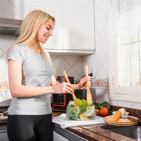 Blonde Jeune Femme Mélangeant Salade Avec La Spatule En Bois Dans L ustensile En Verre Photo