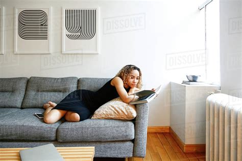 Mixed Race Woman Laying On Sofa Reading Book Stock Photo Dissolve