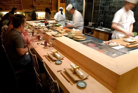 Chefs Preparing Food In A Restaurant Kitchen With People Sitting At The