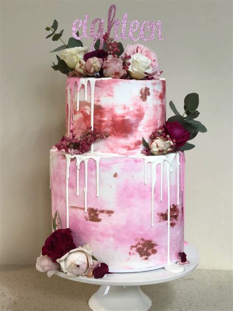 A Three Tiered Cake With Pink And White Icing Dripping Down The Side Topped With Flowers