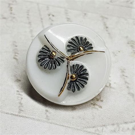 A White And Black Brooch With Two Flowers On Its Side Sitting On A Table