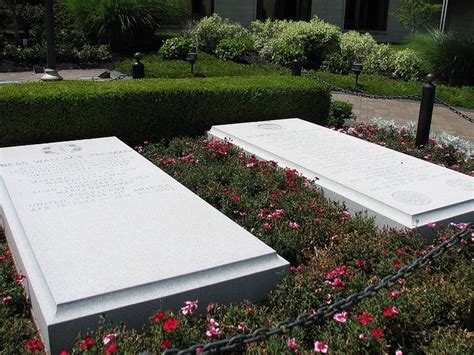 Two White Headstones Are In The Middle Of Some Bushes And Flowers With