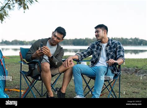 Gay LGBTQIA Couple Sitting On Picnic Chair Drinking Tea And Coffee