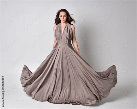 Portrait Of A Pretty Brunette Girl Wearing A Long Silver Evening Gown Full Length Standing Pose